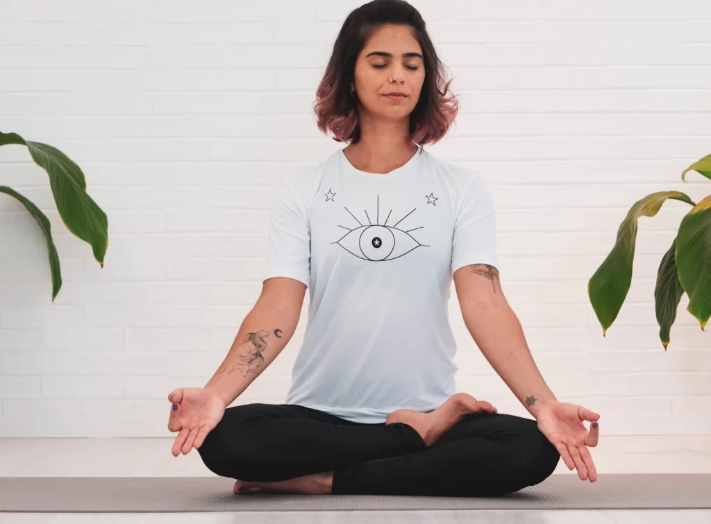 woman in white t-shirt and black pants sitting practicing pranayama technique