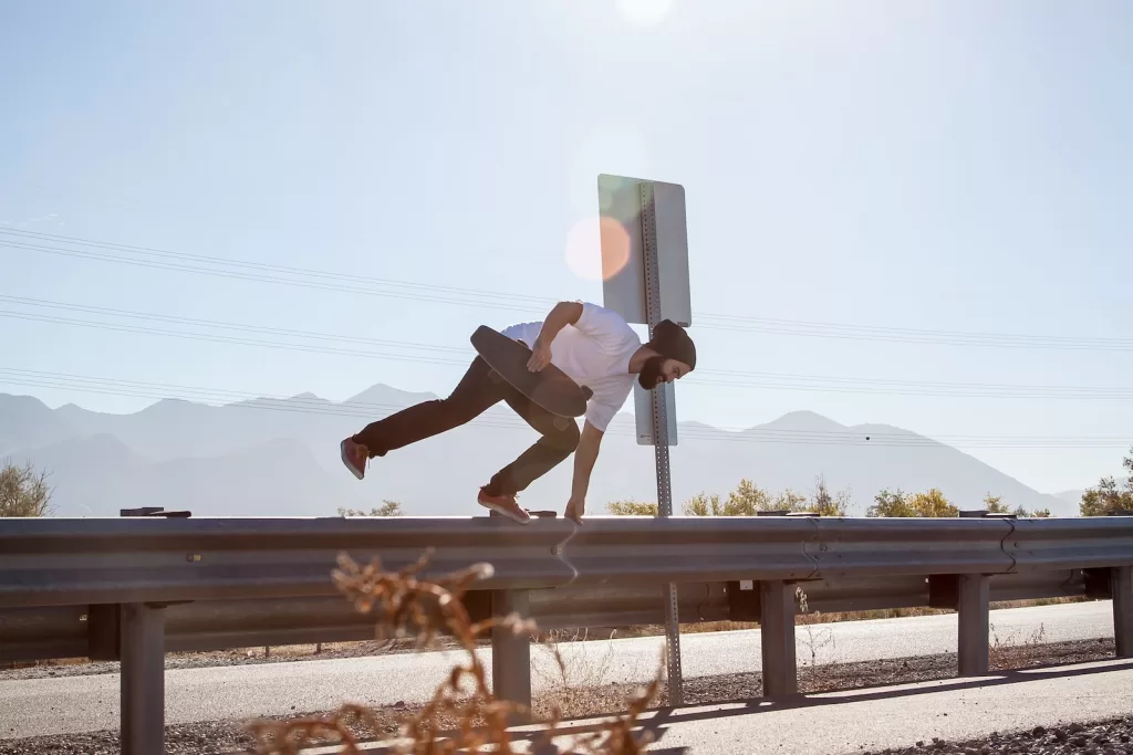 man crossing on road fence while holding black skateboard